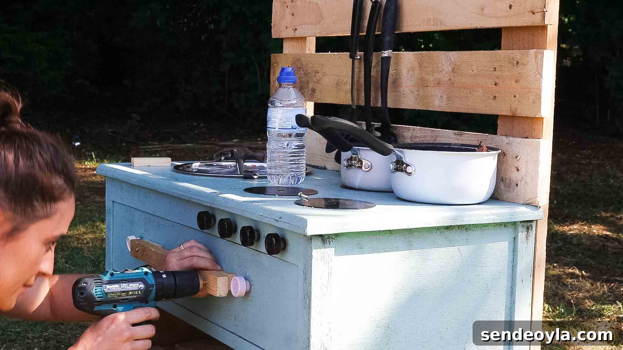 Female woodworker screwing on a towel rack for an upcycled cooking toy space for kids