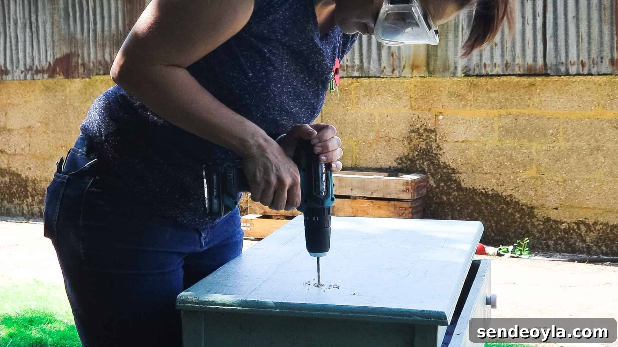 Woman drilling a hole before cutting with a jigsaw for a round washing up bowl in a DIY country kitchen for outside