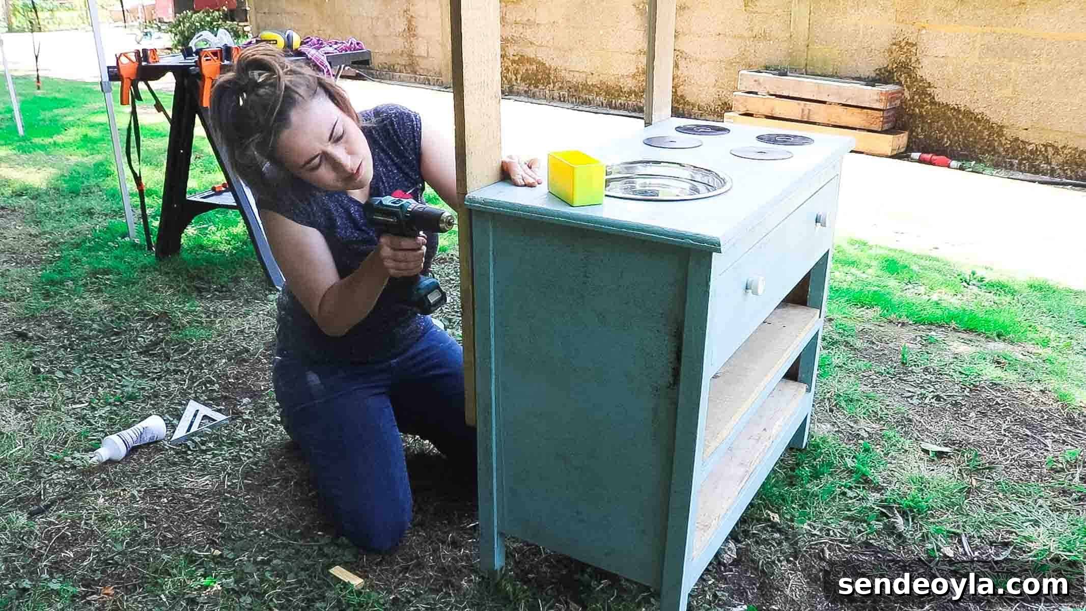Woman screwing pallets on the back of old shabby chic furniture to make a DIY garden bar