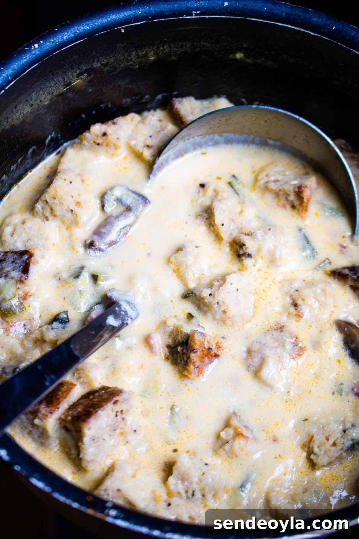 Hearty Cheesy Bacon and Chorizo Bread Soup Recipe 7 Close up of a ladle in a pan of cheesy bacon soup with York bread chunks.