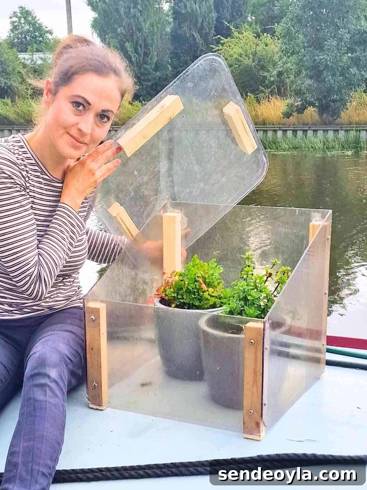 woman holding a plastic clear lid showing the inside of her free homemade cold frame on top of a narrowboat full of mint and parsley