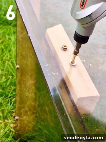 person screwing stop blocks to a cold frame clear lid to stop it from slipping off