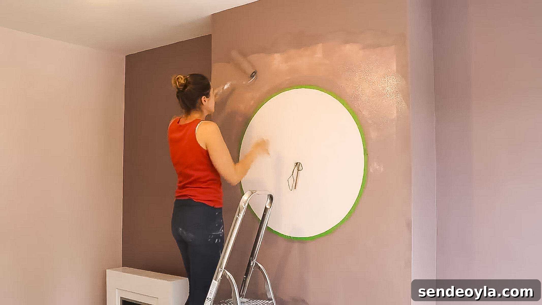 How to Decorate a Room: Practical Tips for Beginners 4 woman painting a circle feature on a chimney breast above a fire place with Dulux heart wood and a pink with a frog masking tape