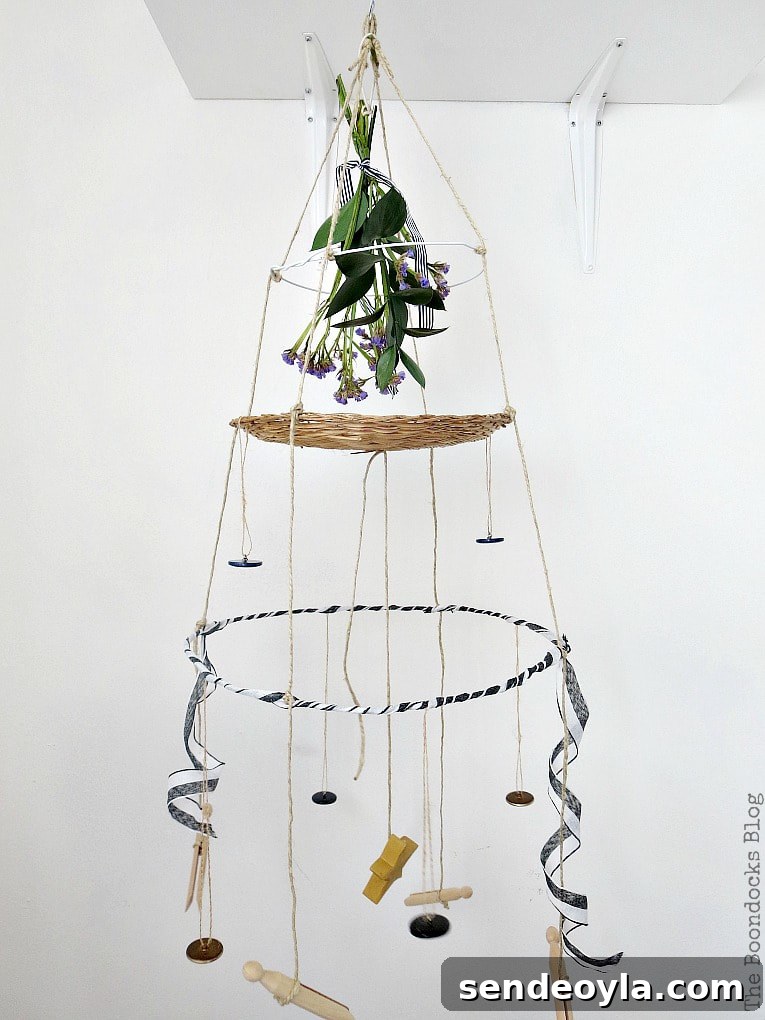 Completed mobile hanger with three tiers made with wire hangers, a wicker charger and twine, embellished with buttons, ribbon and a bouquet.