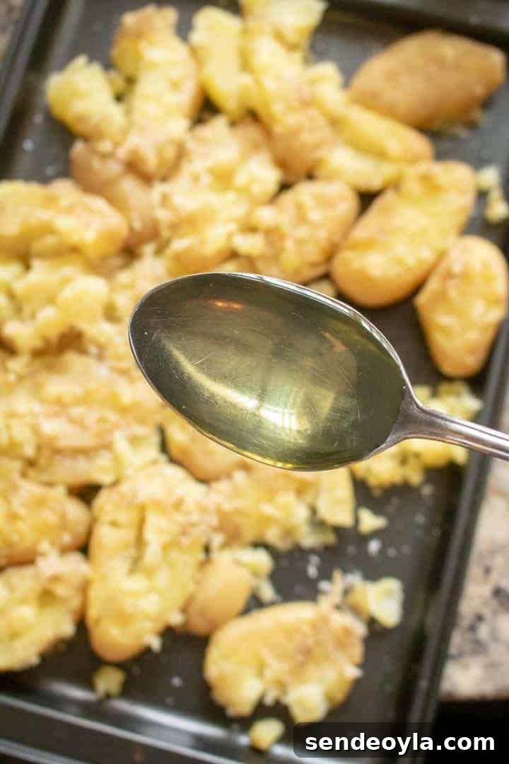 Drizzling olive oil on crushed potatoes laid on a baking tray