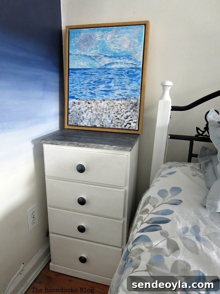 Finished nightstand makeover next to a bed and decorated with a painting.