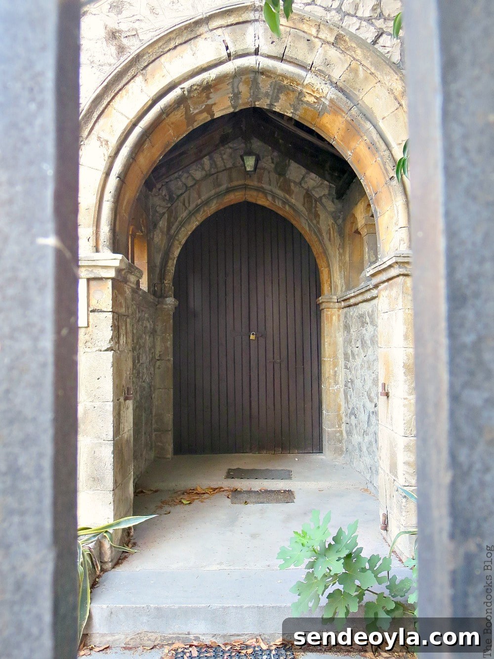 Arched wood door inside stone looked at through fence