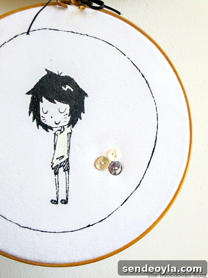 DIY T-Shirt Wall Art: Transform a Tee into Home Decor 10 Close up of hoop wall art made from an upcycled tshirt. It shows a girl character and three sewn on buttons.