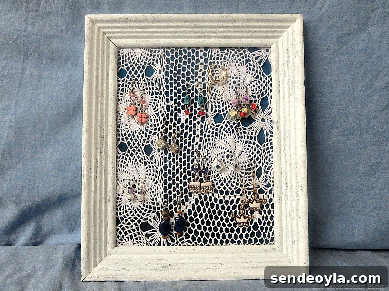 DIY Earring Organizer Ideas to Declutter Your Jewelry 11 The finished earring organizer made with a frame, a blue satin blouse and a doily.