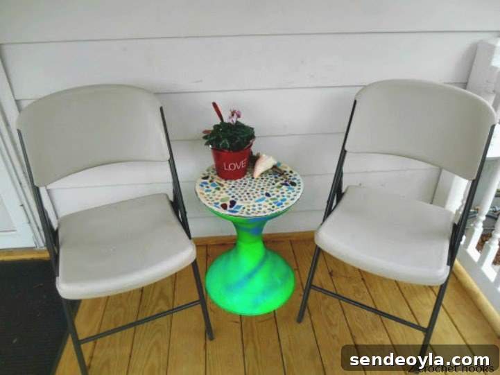 Finished sea glass mosaic table top next to two folding chairs.